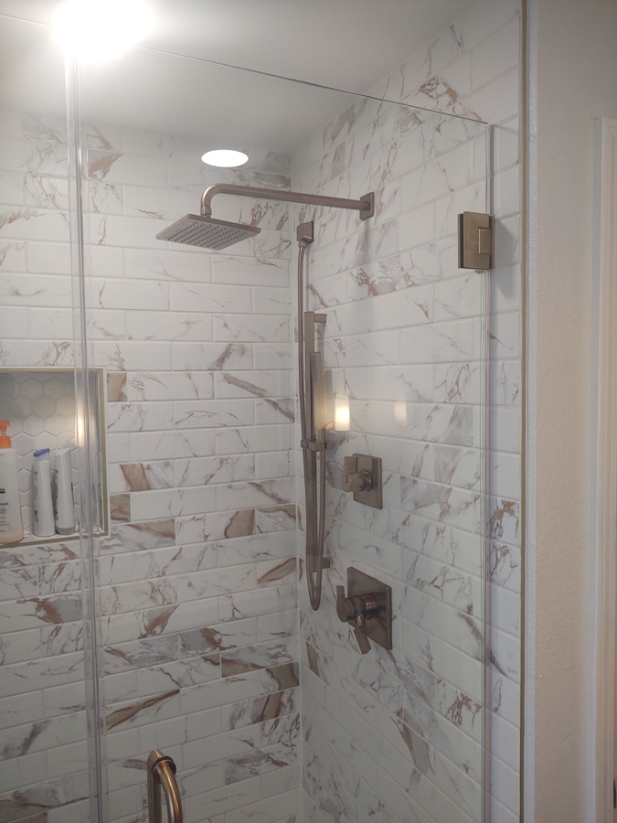 Tile shower with stainless fixtures and rain shower head with 
        additional handheld shower.